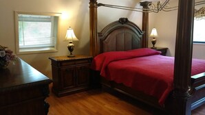 Un lit à baldaquin avec une couvre-lit rouge, des tables de chevet en bois avec des lampes, une fenêtre avec des stores et un plancher en bois.