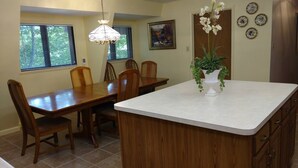 Un coin repas avec une table et des chaises en bois, un îlot central blanc orné d’un vase de fleurs et un tableau accroché au mur.