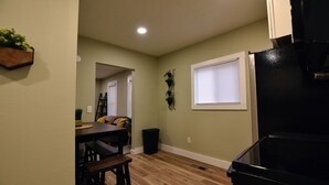 A kitchen with a black refrigerator, wooden flooring, a dining table with chairs, and a window with blinds.