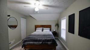 A bedroom with a bed, a ceiling fan, a mirror, and a window.