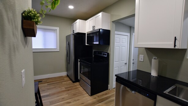 A compact kitchen with white cabinets, a black refrigerator, a microwave, and a dishwasher.