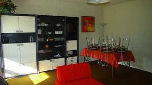 Un comedor con una mesa lista para cuatro, una silla roja y una cocina con armarios y un refrigerador.