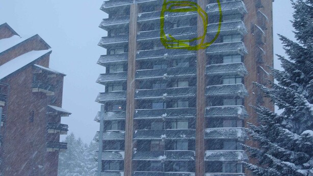 Un edificio de varios pisos con balcones, rodeado de árboles cubiertos de nieve y un suelo nevado.