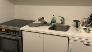 Una cocina compacta con armarios blancos, estufa, pileta y heladera pequeña.