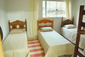 Cozy bedroom with two single beds, each with a wooden headboard and white bedspread, offering a view of the outside through a window.