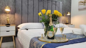 A neatly arranged bedroom with a bed, bedside tables, a vase with yellow flowers, a bottle of Korbel wine, and two glasses.