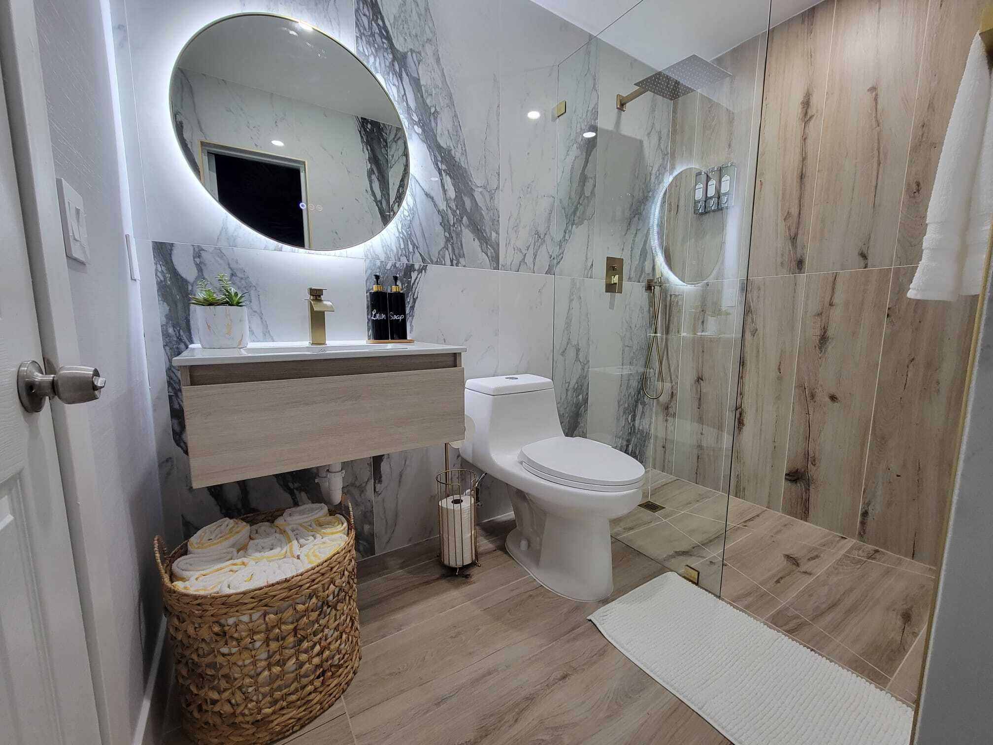 A modern bathroom with a marble vanity, a toilet, a shower with a glass enclosure, and a wicker basket.