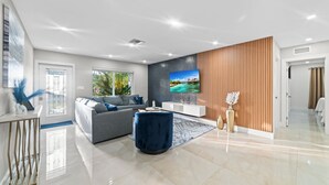 A modern living room with a grey sofa, a blue ottoman, a flat-screen TV, and a wooden accent wall.