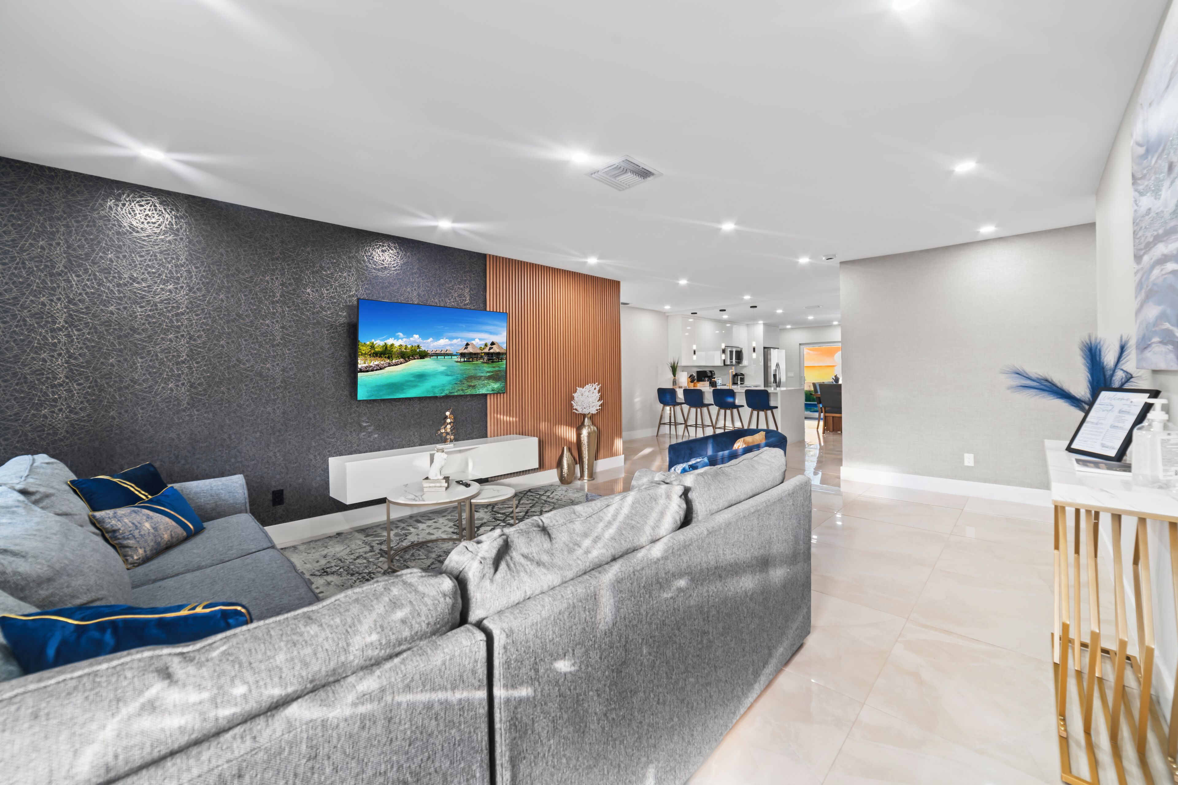 A modern living room with a large sectional sofa, a flat-screen TV mounted on a textured wall, and a minimalist coffee table.