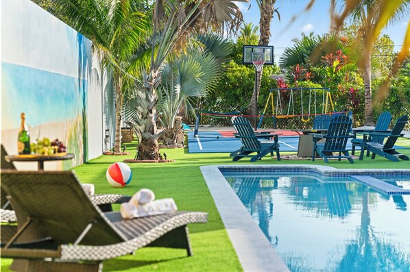 A pool area with lounge chairs, a basketball hoop, and a hammock.