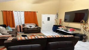 A living room with a sofa set, a television mounted on the wall, and a door in the background. - Luxe Escape Residential Housing (Portmore)