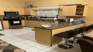A kitchen with a central island, bar stools, a microwave, oven, and a patterned backsplash. - Luxe Escape Residential Housing (Portmore)