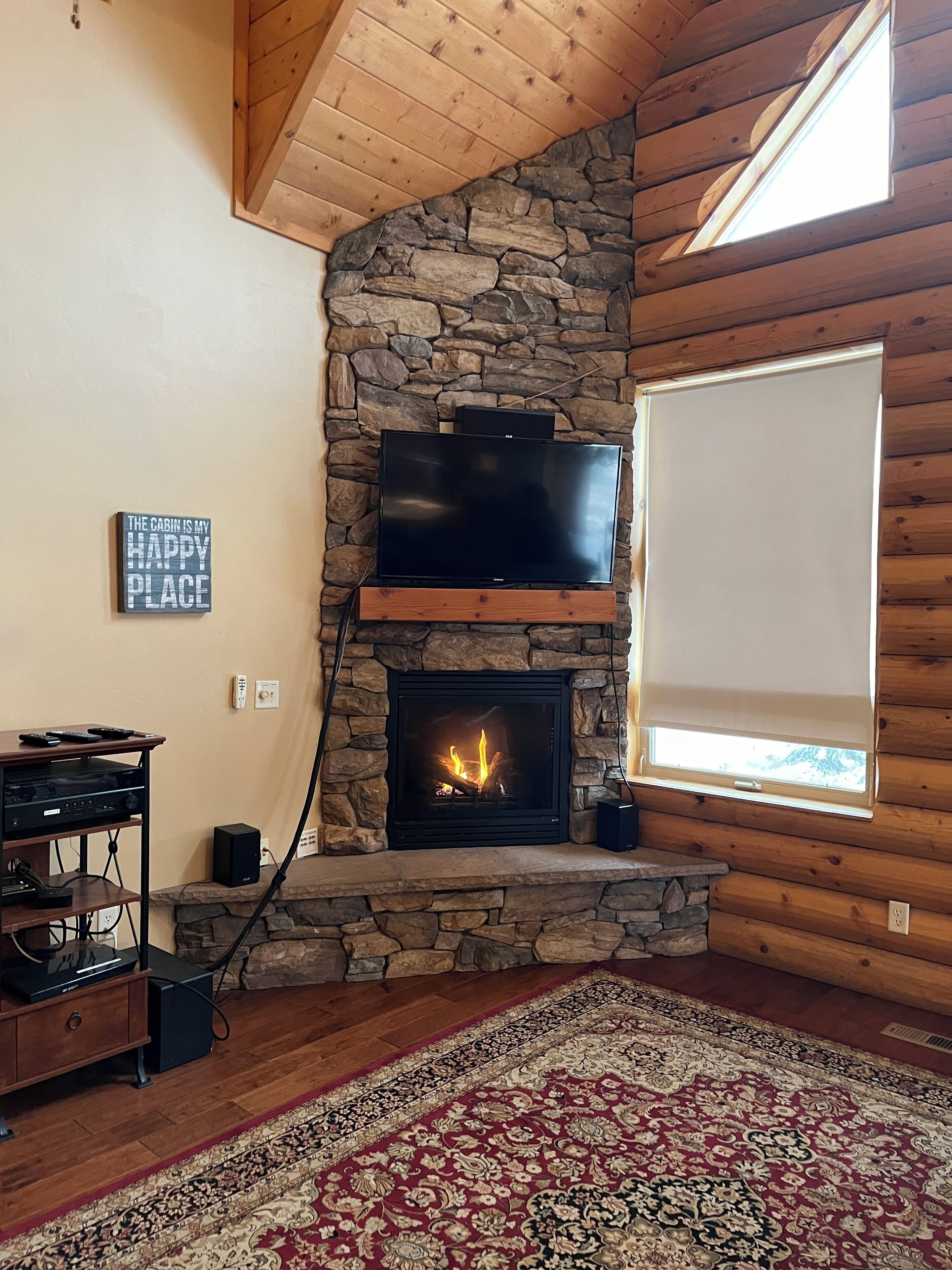 Un intérieur de chalet chaleureux avec une cheminée en pierre, un téléviseur à écran plat fixé au mur et un meuble de rangement en bois.