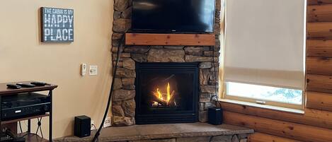 Un intérieur de chalet chaleureux avec une cheminée en pierre, un téléviseur à écran plat fixé au mur et un meuble de rangement en bois.