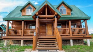 A log cabin with a green roof, a front porch with railings, and a stone foundation.