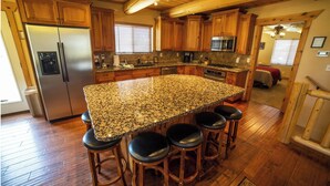 A spacious kitchen with a granite island, wooden cabinets, and a stainless steel refrigerator.