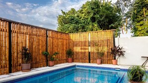 Una piscina con cerramiento de bambú, plantas en macetas y un cielo azul despejado.