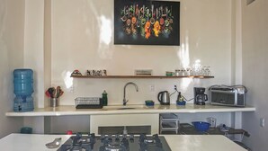 Una cocina moderna con estufa a gas, un lavamanos y una encimera. En la encimera hay un dispensador de agua, una cafetera y un tostador. Un estante sobre la encimera contiene varios utensilios de cocina.
