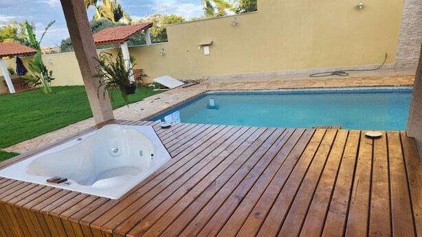 Een houten terras met een jacuzzi en een zwembad.