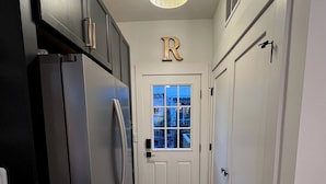 A narrow hallway with a refrigerator, a door with a 'R' sign, and a window with a view of buildings.