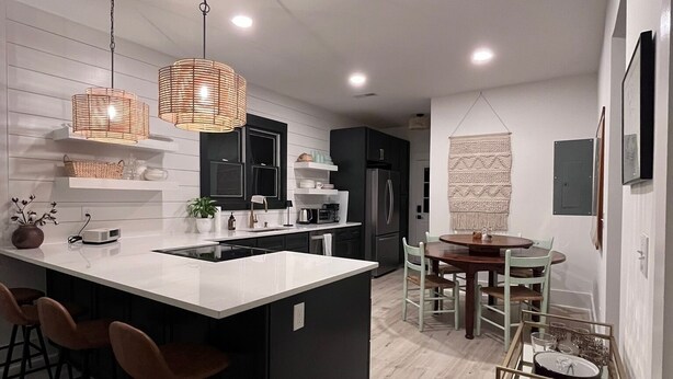 A modern kitchen with a central island, bar stools, pendant lighting, and a dining area with a table and chairs.