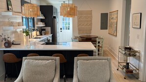 A modern kitchen with a central island, two grey armchairs, pendant lighting, and a dining area with a table and chairs.