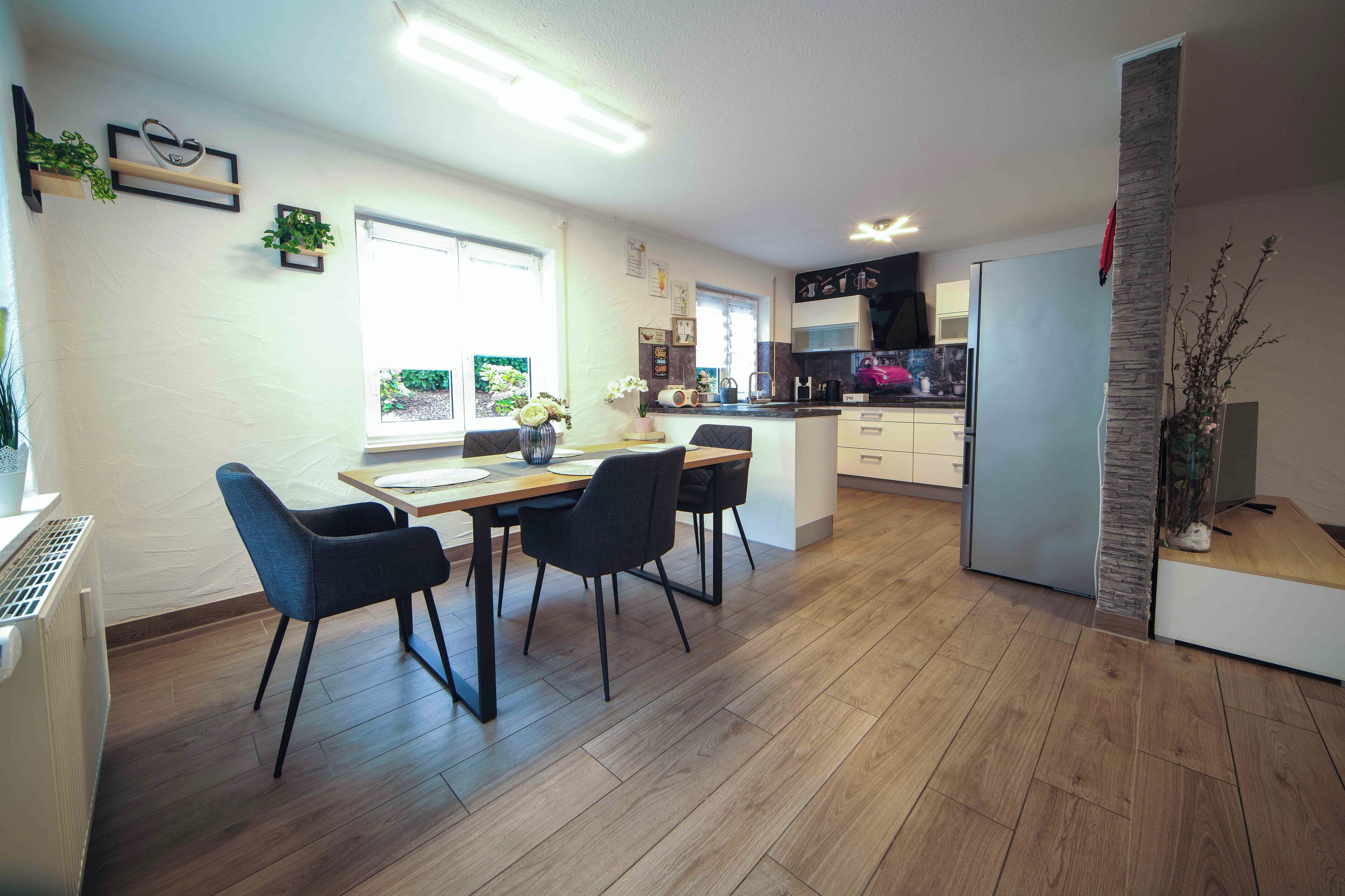 Una cucina moderna con pavimento in legno, un'area pranzo con tavolo e sedie e un frigorifero.