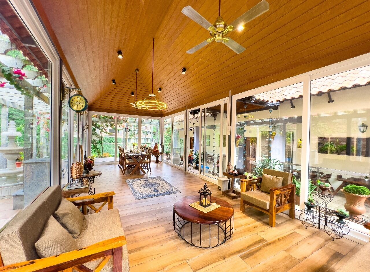 Un espace intérieur spacieux doté d’un plancher en bois, d’un ventilateur de plafond et de grandes fenêtres offrant une vue sur la verdure.