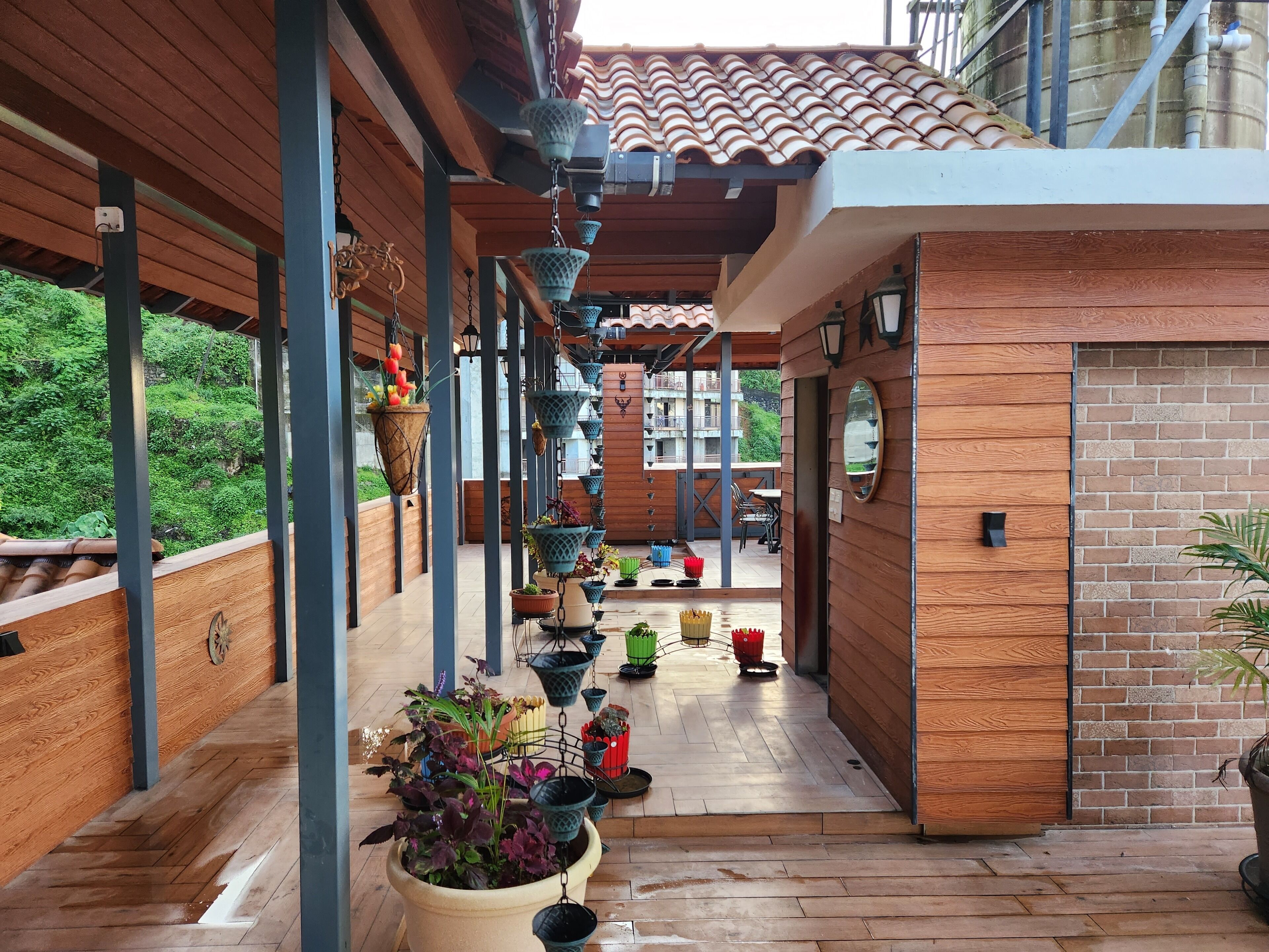 A covered outdoor area with wooden flooring, potted plants, and hanging lanterns.