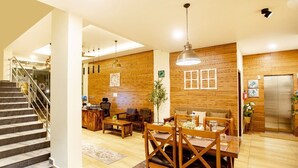 A spacious living area with a wooden wall, a dining table with chairs, a staircase, and a kitchen area with a refrigerator. - Kacholam Serviced Villa (Devikolam)