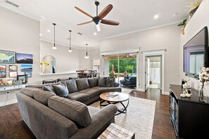 A spacious living room with a sectional sofa, a coffee table, pendant lights, and a ceiling fan.
