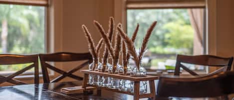 A dining table with a glass vase centerpiece containing pampas grass, set on a wooden stand.
