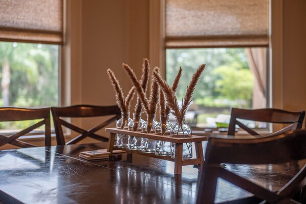 Una mesa de comedor con un centro de mesa de vidrio con plumas de pampa, sobre un soporte de madera.