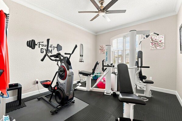 Un gimnasio en casa con equipo de ejercicio, un ventilador de techo y un adhesivo de pared motivacional.