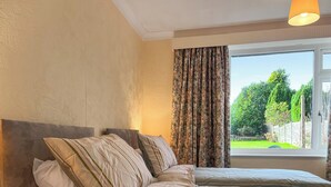 A bedroom with a bed, curtains, and a window with a view of greenery. - 2 bedroom accommodation in Stoke-on-Trent (Stoke-on-Trent)