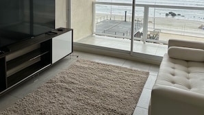Una sala de estar moderna con un televisor de pantalla plana, un sofá color crema y un ventanal con vistas a la playa.