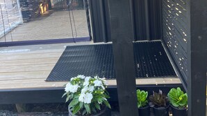 Eine Holzterrasse mit einem schwarzen Grill, einem Topfpflanzen und einem Metallrost.