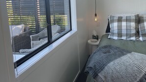 Ein Schlafzimmer mit großem Fenster, einem Bett mit Karo-Bettwäsche, einem Nachttisch und einer Pendelleuchte.