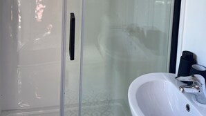 Ein modernes Badezimmer mit einer Duschkabine aus Glas, einem weißen Waschbecken und einem schwarzen Handtuchhalter.