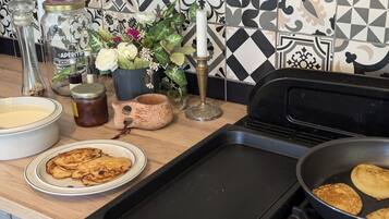 Un bancone della cucina con una padella, una pila di pancake, una ciotola di pastella e diversi utensili da cucina.
