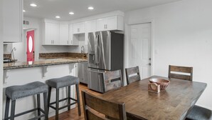 Una cocina moderna con armarios blancos, un refrigerador de acero inoxidable y una mesa de comedor de madera con taburetes de bar.