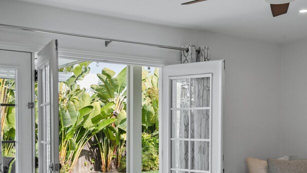 Una sala de estar moderna con un ventanal corredera que da a un patio, un ventilador de techo y un sofá beige.