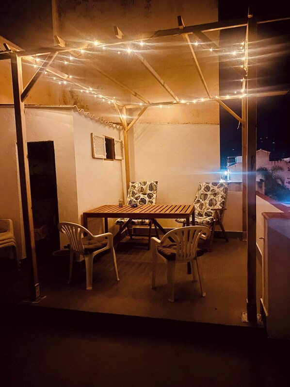 An outdoor patio with a wooden table and chairs, string lights, and a view of the city at night. - Casita Mezcal, in City Center With Great Views (Almunecar)