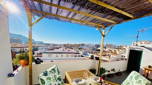 A balcony with a table set for dining, surrounded by potted plants and a view of the cityscape. - Casita Mezcal, in City Center With Great Views (Almunecar)