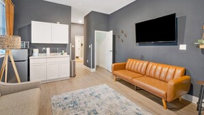 Een moderne woonkamer met een bank, een flatscreen televisie en een keuken met witte kasten.
