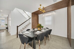 Een eetruimte met een lange tafel gedekt voor zes personen, een houten plafond en een trap op de achtergrond.