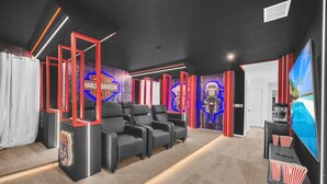 Une salle de cinéma maison avec des fauteuils inclinables en cuir noir, un grand téléviseur à écran plat et un mur décoré sur le thème de Harley-Davidson.