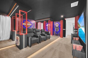 Une salle de cinéma maison avec des fauteuils inclinables en cuir noir, un grand téléviseur à écran plat et un mur décoré sur le thème de Harley-Davidson.
