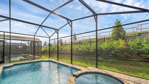 Une piscine avec un jacuzzi, entourée d’une structure en verre, et offrant une vue sur un paysage verdoyant.