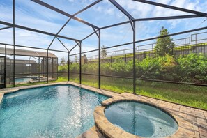 Une piscine avec un jacuzzi, entourée d’une structure en verre, et offrant une vue sur un paysage verdoyant.